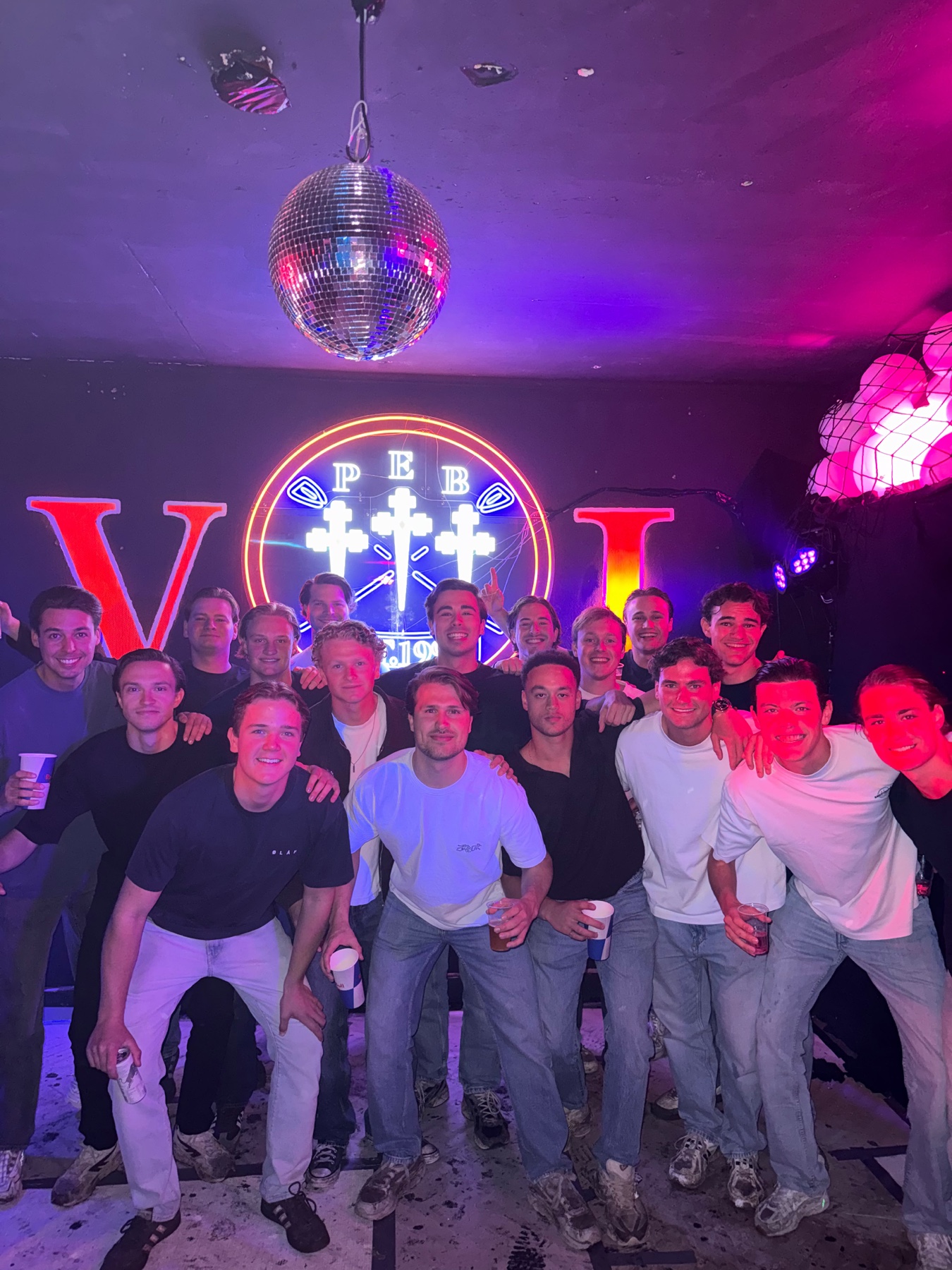 Leden op het huischfeest onder de discobal en het verlichte P.E.B.-wapen